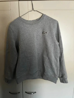 Womens Lacoste Sweater - Grey Lacoste sweatshirt in excellent condition. Size 👕: Women’s M / 38 / 10 ✅ Authentic product. Feel free to ask for more photos or measurements if you have any questions! 📦 Fast shipping: within 24 hours of purchase.