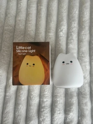 Söt nattlampa i silikon kattform - En vit nattlampa i mjuk silikon formad som en katt med gulligt ansikte och rosa kinder. Lampan lyser i olika nyanser, eller i vanligt gult sken och styrs genom att trycka på den. Perfekt som mysbelysning eller dekoration i rummet.