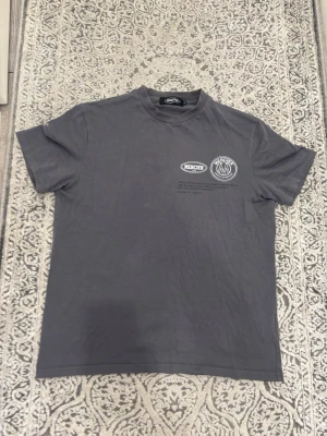 Grå t-shirt från Mercier - Snygg grå t-shirt från Mercier med tryck på bröstet. Klassisk passform och rund hals. Tillverkad i mjuk bomull som känns skön mot huden. Perfekt för en avslappnad och stilren look.