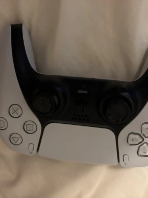 Sony DualSense PS5 handkontroll vit - Säljer en Sony DualSense handkontroll till PlayStation 5. Den är vit med svarta detaljer och har en modern, ergonomisk design. Tillverkad i plast med touchpad, adaptiva triggers och inbyggd mikrofon. Perfekt för gaming på PS5. Den är helt perfekt Inga skador
