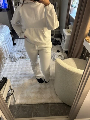 Vit hoodie och mjukisbyxor set - Säljer ett vitt loungewear-set med hoodie och matchande mjukisbyxor. Hoodien har känguruficka och dragsko i huvan, byxorna har resår och dragsko i midjan. Perfekt för chill dagar hemma eller när du vill vara extra bekväm. På sista bilden kan du se en liten liten fläck som knappt syns, inte försökt få bort det men gå säkert bort med vanish!