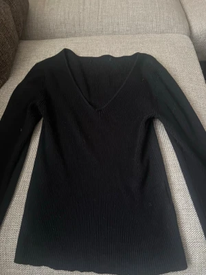 Svart ribbad långärmad topp - Snygg svart ribbad topp med lång ärm och djup V-ringning. Materialet är stretchigt och sitter tajt mot kroppen, perfekt för att styla med jeans eller kjol. Enkel och stilren design utan tryck eller detaljer. Pris kan diskuteras 💞💞