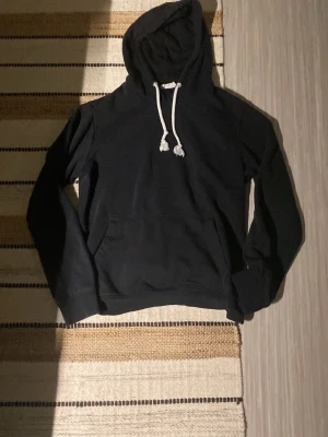 Svart hoodie från Pier One - Svart hoodie från Pier One med vit dragsko och klassisk känguruficka framtill. Mjuk bomullskänsla och huva som ger en avslappnad look. Perfekt för chill dagar eller när du vill ha något bekvämt och stilrent.