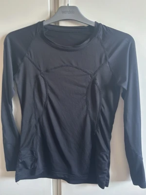 Svart långärmad träningströja - Svart långärmad träningströja med rund hals och markerade sömmar för en sportig look. Tillverkad i ett stretchigt och lätt material som passar perfekt för träning eller löpning. Snygg passform och stilren design.