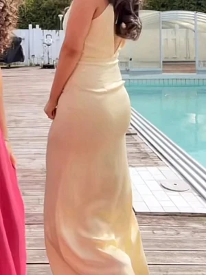 Gul långklänning - Elegant långklänning i champagnefärg med figurnära passform och ärmlös design. Klänningen har en mjuk, slät yta och en klassisk siluett som ger en stilren look. Perfekt för speciella tillfällen.