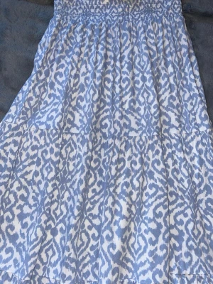 Blåvit mönstrad sommarklänning 157 - Ljusblå och vit klänning från 157 med smock upptill och ett snyggt abstrakt mönster. Klänningen har en luftig passform och är perfekt för varma dagar. Tillverkad i ett mjukt och lätt tyg som känns skönt mot huden.