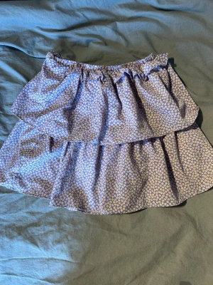 Lila blommig volangkjol  - Supersöt kort volangkjol från SHEIN i lila med små vita och röda blommor. Kjolen har dubbla volanger och resår i midjan för en bekväm passform. 