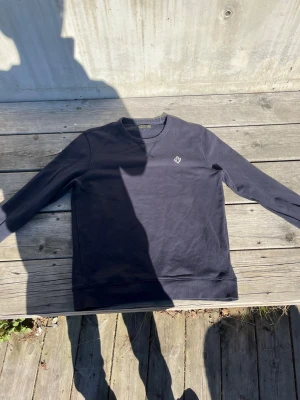 Mörkblå sweatshirt från Morris - Snygg mörkblå sweatshirt från Morris med rund halsringning och diskret logga broderad på bröstet. Tröjan har ribbade muddar vid ärmslut och nederkant, perfekt för en avslappnad och stilren look. Tillverkad i mjuk bomull.