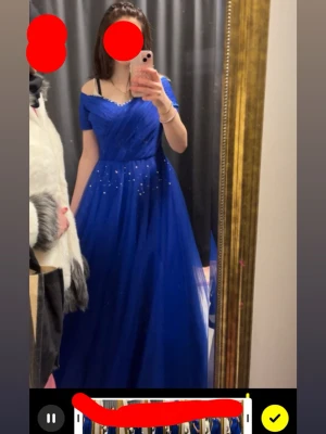 Blå långklänning med pärlor - Elegant blå långklänning med offshoulder-design och pärldetaljer på kjolen. Klänningen har ett flödande tyg som ger en lyxig känsla och passar perfekt för speciella tillfällen. Materialet ser ut att vara polyester och klänningen har en vacker v-ringning. Priset går att diskuteras