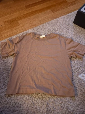 Beige basic t-shirt från Gina Tricot - En enkel och stilren beige t-shirt från Gina Tricot, basically basics-kollektionen. T-shirten har rund halsringning och korta ärmar, perfekt för en clean och avslappnad look. Tillverkad i mjuk bomull för skön känsla hela dagen.