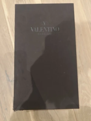 Valentino Garavani Box - Säljer ett exklusivt väsktillbehör från Valentino Garavani. Inkluderar original ask, dustbag och en liten svart accessoar. Perfekt för dig som gillar lyxiga detaljer och vill komplettera din väska med något extra. En liten defekt på lådan som knappast syns. Vid snabb affär kan priset ändrats!