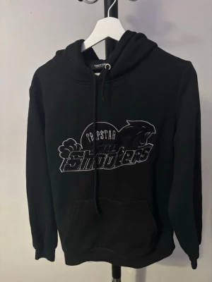  Trapstar hoodie  - Säljer en svart hoodie från Trapstar med stort 'Shooters' tryck och pantermotiv på bröstet. Klassisk huva med dragsko och magficka framtill. Perfekt för dig som gillar streetwear och vill ha en stilren men ändå unik look.