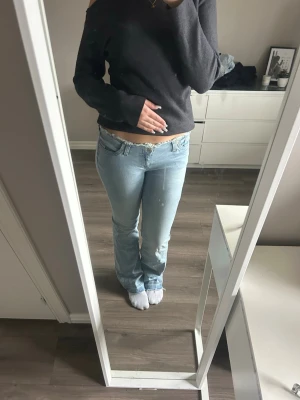 Ljusblå bootcut jeans från Nelly - Säljer ett par ljusblå bootcut jeans med låg midja. Inget synligt märke på jeansen. Materialet är denim i bomull. Slitningar i midjan och längst ner på benen. 