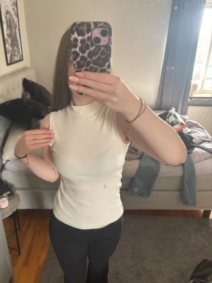 Vit stickad ärmlös topp - Säljer en stilren vit stickad topp med hög hals och ärmlös design. Toppen har en tight passform och är stretchig❤️Smutsig spegel därav fläcken som ser ut att vara på tröjan!