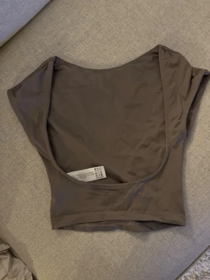 Topp med öppen rygg - Snygg brun  topp med öppen rygg från Bershka. Tillverkad i mjuk och stretchig polyesterblandning som sitter skönt mot kroppen. Perfekt att styla med jeans eller kjol för en trendig look. En liten deofläck som inte gick bort i vanlig tvätt men går säkert bort med medel. I storlek XS.
