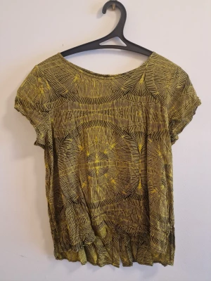 Mönstrad gul och svart blus från Monki - Snygg blus från Monki i gult och svart med grafiskt mönster. Blusen har rund halsringning och korta ärmar. Luftig och skön modell som passar perfekt till jeans eller kjol.