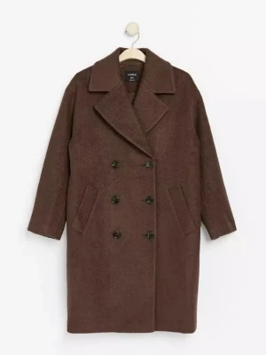 Brun ullkappa med knappar - Mysig brun kappa från Lindex i ullmix med rak passform och stora knappar framtill. Kappan har hög krage, två sidofickor och ett mjukt, texturerat tyg. Perfekt för kyliga dagar och ger en stilren look.