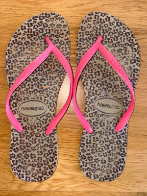 Havaianas sandaler leopardmönster rosa - Coola flip-flops från Havaianas med leopardmönstrad sula och starkt rosa remmar. Perfekta för sommaren. Mjukt och flexibelt gummimaterial som är skönt att gå i. Snygg detalj med Havaianas-logga på remmarna.