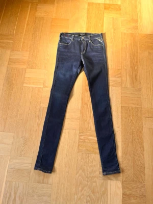 Mörkblå skinny jeans från Replay - Snygga mörkblå skinny jeans från Replay med klassisk femficksdesign och kontrastsömmar. Jeansen har en smal passform och stretchigt material som sitter tajt längs benen. Perfekta för en trendig och avslappnad stil.