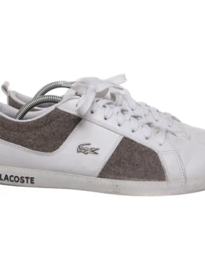 Stiliga Lacoste Sneakers - Snygga sneakers från Lacoste i vitt och gråbrunt med klassisk låg profil. Skorna har vita skosnören, grå textilpaneler på sidorna och detaljer i vitt läder. Ikoniska Lacoste-loggan i silver på sidan och text på sulan. Perfekta för en clean och stilren look.