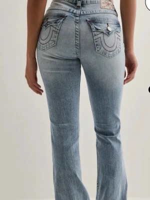Ljusblå bootcut jeans True Religion - Säljer ett par ljusblå bootcut jeans från True Religion med slitningar på låret och knät. Jeansen har klassiska bakfickor med dekorativa sömmar och knappdetaljer. Tillverkade i denim med en skön passform och mid waist. (Pris går att diskutera)