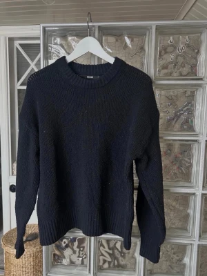 Svart stickad tröja från bikbok - En stilren svart stickad tröja från bikbok med rund halsringning och ribbade muddar. Tröjan har en avslappnad passform och är perfekt för lager-på-lager. Materialet känns mjukt och håller värmen under kyliga dagar.