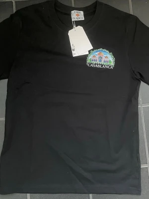 Svart Casablanca t-shirt med tryck - Snygg svart t-shirt från Casablanca med färgglatt tryck av byggnader och gröna detaljer både fram och bak. T-shirten har rund hals och korta ärmar. Tillverkad i mjuk bomull för skön känsla och stilren look.