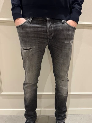 Grå slitna jeans - Säljer ett par sjysta grå skinny jeans med slitningar och tvättade detaljier från Jack & Jones. Använda sparsamt alltså inga tecken på användning. Vid minsta fundering tveka inte på att höra av dig. 