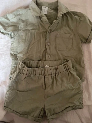 Beige set med skjorta och shorts H&M - Snyggt set från H&M i beige bomullstyg. Setet består av en kortärmad skjorta med krage, bröstficka och knappar framtill samt matchande shorts med resår i midjan. Perfekt för en avslappnad och trendig look.