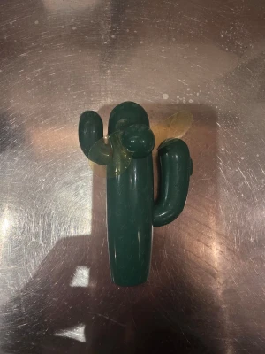 Grön kaktusformad plastleksak - Rolig grön plastleksak formad som en kaktus med två gula propellerblad på ena sidan. Leksaken har rundade former och detaljer som liknar taggar på ytan. Perfekt som prydnad eller för lek. Flamingo och kaktus handfläkt.