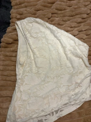 Vit spets topp oneshoulder - Säljer en vit topp i spets med blommigt mönster och oneshoulder-design. Perfekt för dig som vill ha något unikt och stilrent. Tunn och lätt, passar till många olika looks.