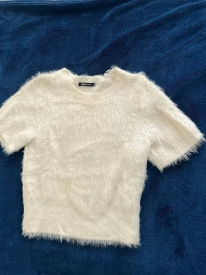 Vit fluffig topp från Gina Tricot - Supersöt vit fluffig topp från Gina Tricot med korta ärmar och rund hals. Toppen har en mjuk och lurvig känsla som ger en trendig look. Perfekt att styla med jeans eller kjol för en cool vibe.