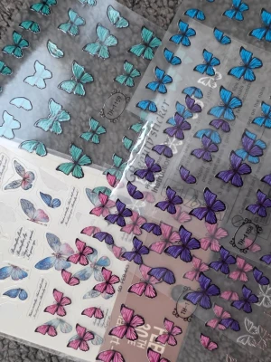 Fjärilsstickers i olika färger - Säljer flera ark med fjärilsstickers i blått, lila, rosa och turkos. Stickersarna är genomskinliga och har detaljerade fjärilsmotiv i olika storlekar och former, perfekta för dekoration av anteckningsböcker, mobilskal eller scrapbooking eller naglar 