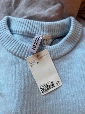 Ljusblå stickad tröja från H&M - (Aldrig använd) Säljer en ljusblå stickad tröja från H&M med rund halsringning och ribbade muddar vid ärmslut och nederkant. Tröjan har en enkel, klassisk design och är perfekt för dig som gillar en clean och stilren look.