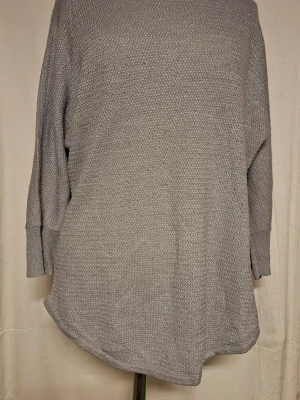 Ljusgrå glittrig stickad oversized tröja - Mysig ljusgrå glittrig stickad tröja med avslappnad, oversized passform och rundad nederkant. Tröjan har långa ärmar med breda muddar och är tillverkad i ett mjukt, grovstickat material. Perfekt för lager på lager och en chill look.