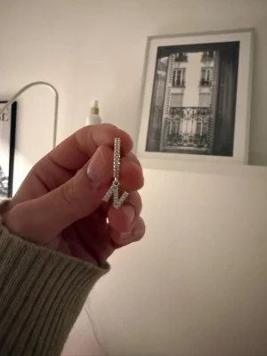 Silverfärgat blixtörhänge från Paku - Säljer ett silverfärgat örhänge från Paku med blixtformad hängande detalj. Örhänget är täckt av små gnistrande stenar som ger en lyxig känsla. Perfekt för dig som vill sticka ut med en cool accessoar.