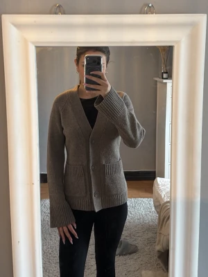 Brun stickad kofta från Wera - Brun stickad kofta med v-ringning och tre knappar framtill. Koftan har två stora fickor och ribbstickade muddar vid ärmslut och nederkant. Knappt använd och inga slitningar, storlek S men passar XS