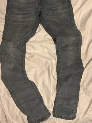 Grå slim fit jeans - Säljer ett par grå slim fit jeans med snygg tvätt och diskreta slitningar. Jeansen har klassisk femficksdesign och smal passform som sitter tajt längs benen. Perfekta för en modern och avslappnad stil.kommer med prislappen 