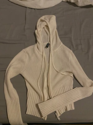 Vit ribbad hoodie med dragkedja - Säljer en vit ribbad hoodie från Bershka med dragkedja framtill och långa ärmar. Hoodien har en croppad passform och är tillverkad i mjukt stickat material. Perfekt för en chill och trendig look.