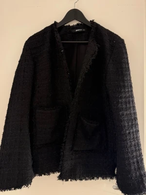 Svart tweedkavaj med råa kanter - Stilren svart kavaj från Gina Tricot i tweedmaterial med råa kanter och två stora framfickor. Rak passform och lång ärm ger en trendig look. Perfekt för dig som gillar en edgy men klassisk stil.