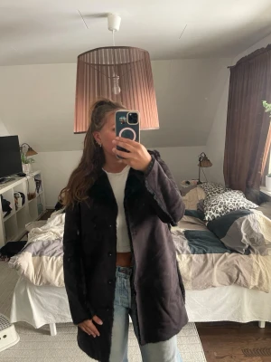 Svart fuskpäls kappa - Snygg svart kappa med fuskpälsdetaljer och bred krage. Kappan har knäppning framtill och är i ett mjukt material som ger en lyxig känsla. 