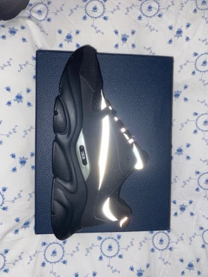 Svarta Dior sneakers med reflexdetaljer - Säljer ett par svarta Dior sneakers med reflekterande detaljer längs sidan och vid tån. Skorna har snörning och är tillverkade i en mix av syntet och skinn. De är storlek 45 men passar för storlek 44. Skriv vid fler bilder eller några frågor 😊