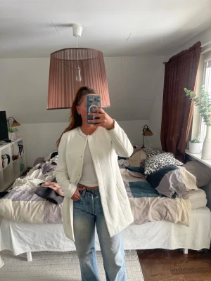 Vit kappa från Jacqueline de Yong - Stilren vit kappa från Jacqueline de Yong i storlek medium. Kappan har rak passform, diskreta fickor och knäppning framtill. 