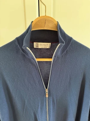 Brunello Cucinelli zip - Snygg blå tröja i kashmir från Brunello Cucinelli med hel dragkedja och ståkrage. Tröjan har en clean look, ribbade muddar och är långärmad. Perfekt för dig som gillar lyxiga och stilrena plagg med premiumkänsla.