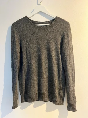 Grå stickad tröja - En enkel och stilren grå stickad tröja med rund halsringning och ribbade muddar vid ärmslut och nederkant. Storlek: XS