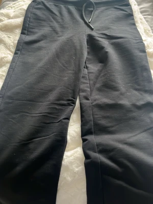 Svarta mjukisbyxor med dragsko - Svarta mjukisbyxor med rak passform och elastisk midja med dragsko. Perfekta för chill dagar och har en enkel design utan logga eller mönster. Materialet känns mjukt och bekvämt, troligen bomull eller bomullsblandning.