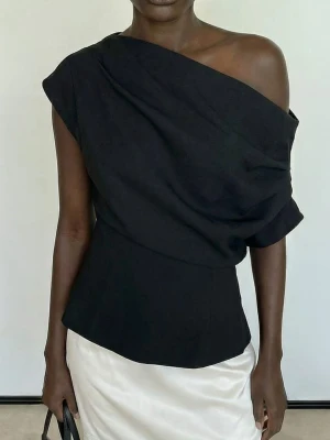 Svart oneshoulder topp - Stilren svart topp med oneshoulder-design och draperad effekt över axeln. Toppen har en figurnära passform och är perfekt för dig som vill ha en trendig och elegant look.