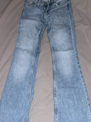 Ljusblå bootcut jeans - Säljer ett par ljusblå bootcut jeans med klassisk femficksdesign och dragkedja med knapp. Jeansen har en lätt tvättad look och raka ben som går ut lite nedtill. Perfekta för en avslappnad och trendig stil. Nya utan prislapp (tvättade endast)