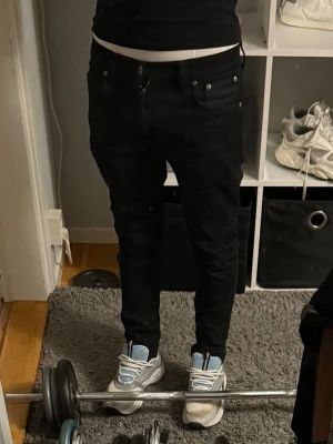 Svarta slim fit jeans från Nudie Jeans - Säljer ett par svarta slim fit jeans från Nudie Jeans. De har klassisk femficksdesign, knappgylf och raka ben. Materialet är stretchigt denim som sitter snyggt och bekvämt. Perfekta för dig som gillar en stilren och modern look. Sitter bra på mig som är 170 passar längre ochkså w28 men mer som 29