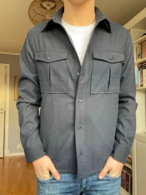Riley overshirt mörkblå – storlek S – helt ny - Stilren overshirt från Riley i storlek S.  Klassisk modell med två bröstfickor och snygg mörkblå färg. Perfekt som lätt jacka över t-shirt eller skjorta.  Helt ny och i mycket fint skick.  Storlek: S Skick: Ny